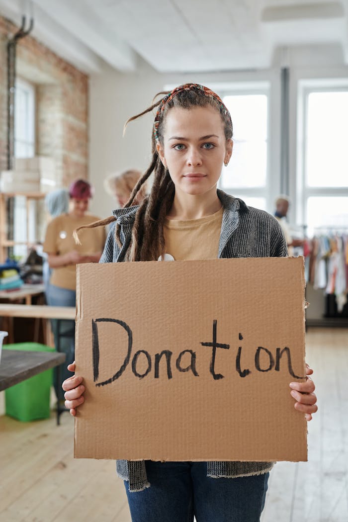 Female volunteer holding a cardboard donation sign in a charity setting.