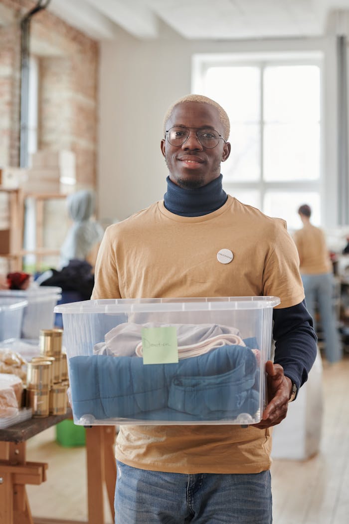 Black man volunteering in thrift store, holding donation box and smiling at camera.